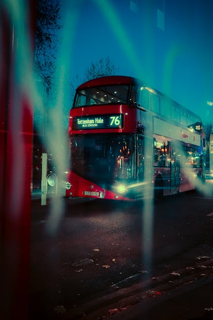 A double-decker bus with a red and cream exterior parked on a street at night, illuminated by streetlights and possibly some ambient urban lighting. The bus is displaying route number 76 with a destin